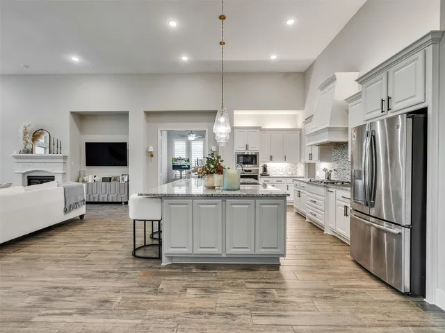 a kitchen with stainless steel appliances granite countertop a refrigerator a sink dishwasher a oven and a large island with wooden floor