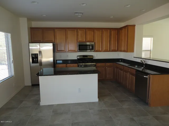 a kitchen with kitchen island granite countertop stainless steel appliances a sink a stove a refrigerator cabinets and a window