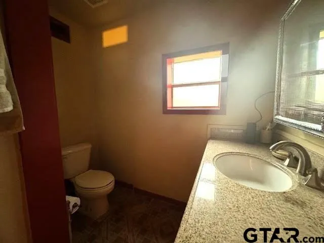 a bathroom with a granite countertop toilet a sink a window and mirror