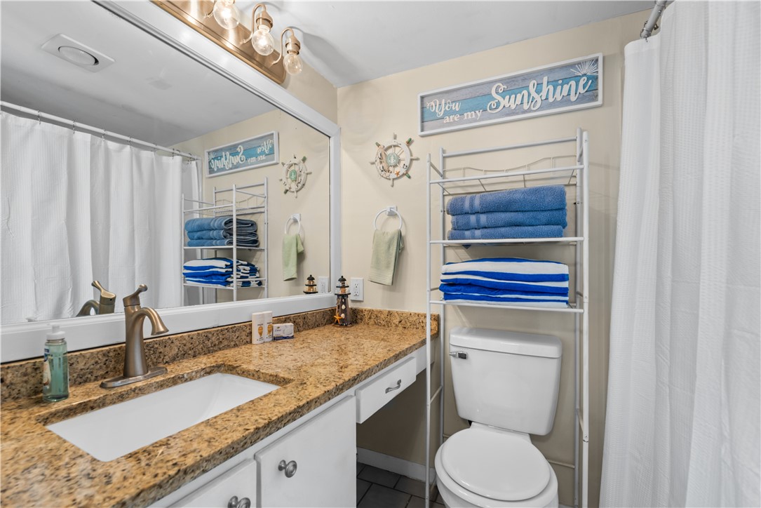 14401 Commodores Drive, Unit 101 Corpus Christi, TX 78418 - Photo 21 of 26 a bathroom with a granite countertop sink a toilet and a mirror