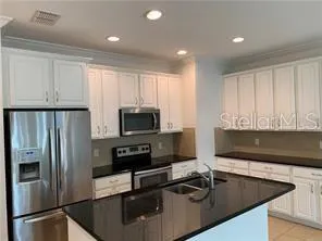 a kitchen with stainless steel appliances granite countertop a refrigerator a stove a sink and white cabinets