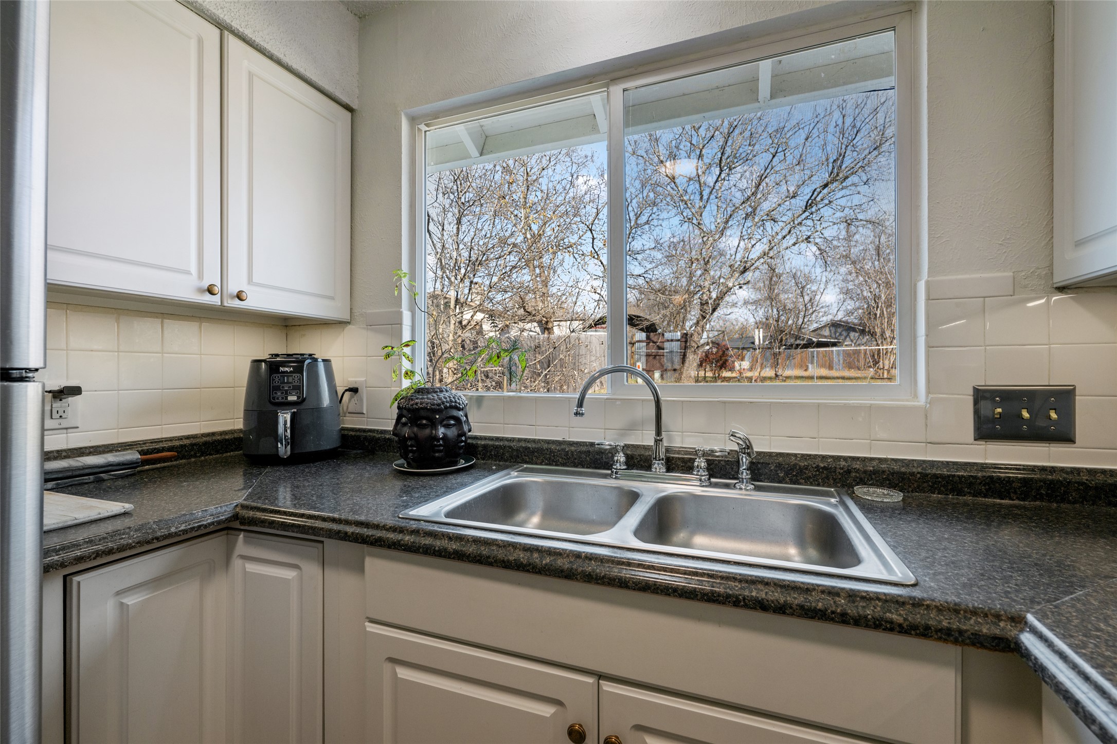 5100 Lambs Lane Austin, TX 78744 - Photo 16 of 31 Kitchen featuring dark countertops, white cabinets, and decorative backsplash.