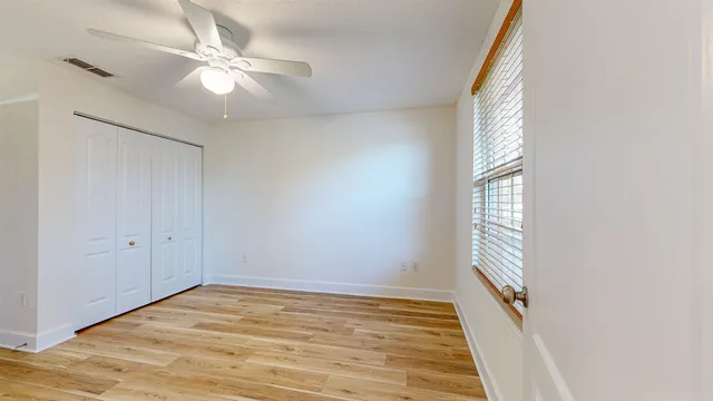 an empty room with wooden floor fan and windows