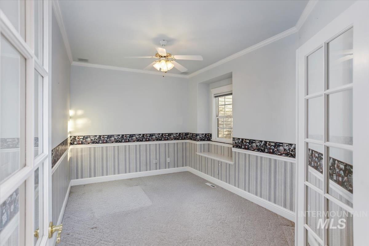 25074 The Driving Lane Caldwell, ID 83607 - Photo 20 of 29 Spare room featuring wainscoting, wallpapered walls, crown molding, light colored carpet, and a ceiling fan