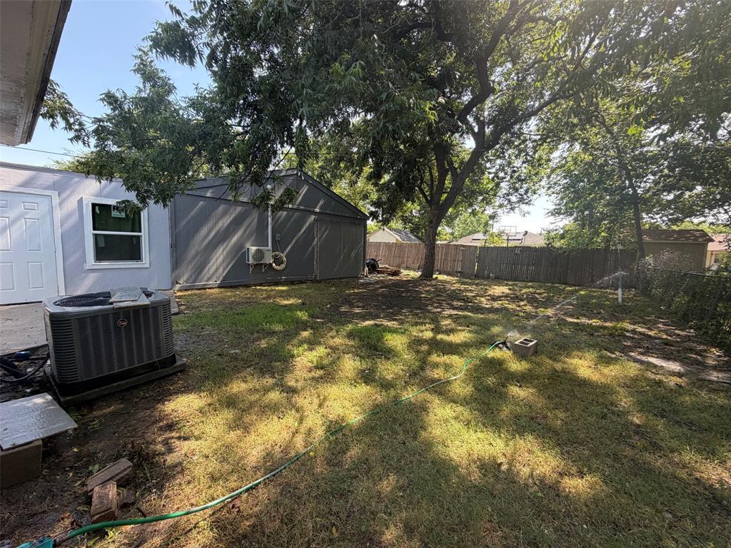 513 Shawnee Trace Grand Prairie, TX 75051 - Photo 32 of 32 Spacious backyard featuring mature trees, a privacy fence, a detached shed, and a separate structure with a white entry door and window