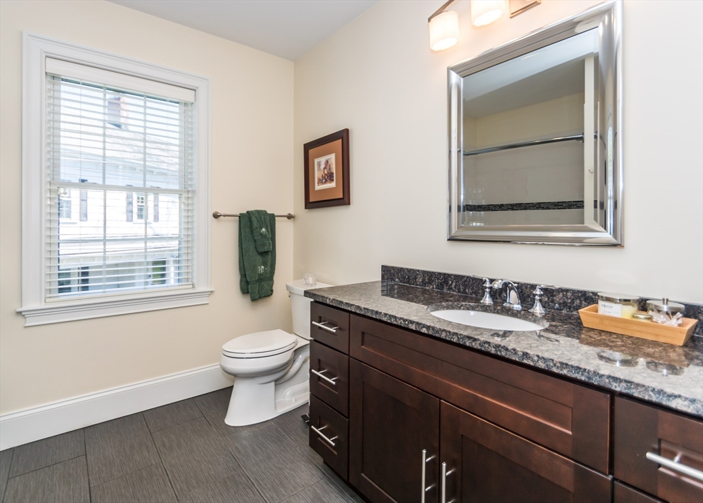 128 Church Street, Unit 2 Waltham, MA 02452 - Photo 20 of 41 a bathroom with a granite countertop toilet a sink and a mirror
