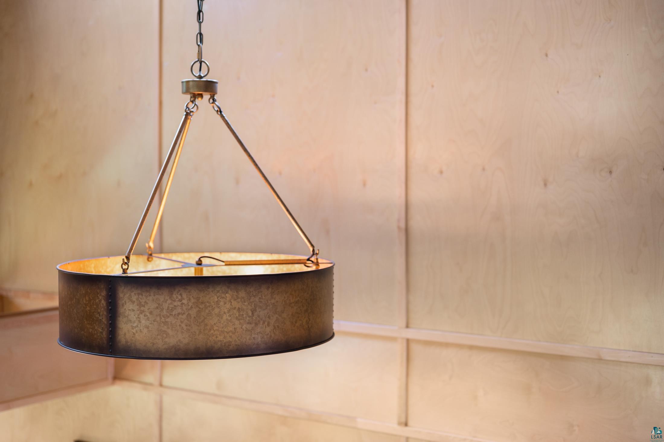 3778 East County Road Barnum, MN 55707 - Photo 34 of 52 Pendant light fixture with a metallic drum shade, suspended by chains and rods, set against a paneled wood-finish wall
