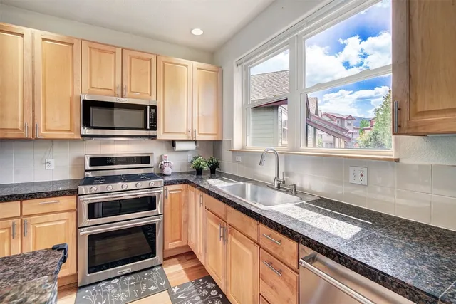 a kitchen with granite countertop a sink cabinets stainless steel appliances and a window