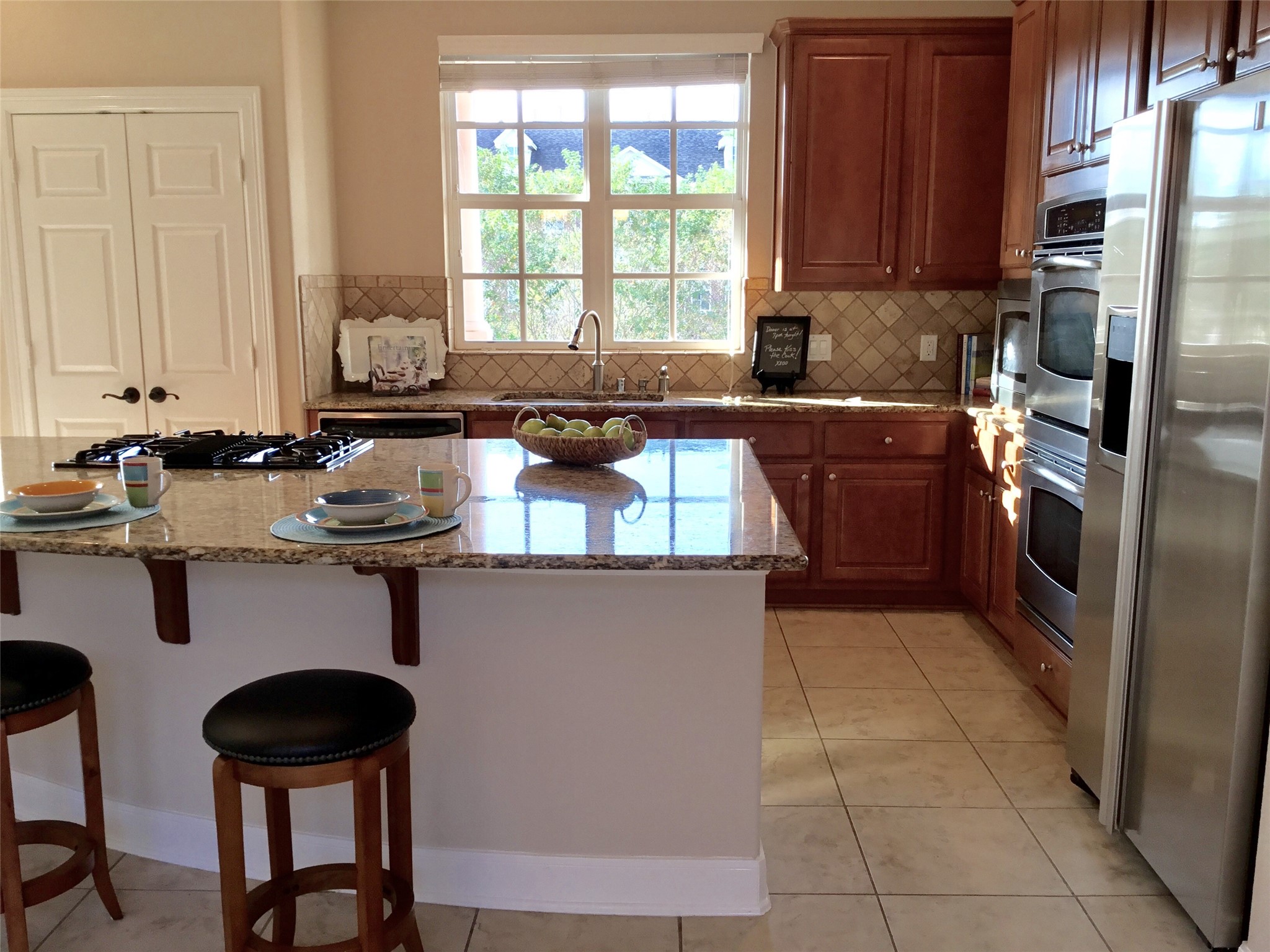 2 Islewood Boulevard Spring, TX 77380 - Photo 14 of 48 This kitchen features granite countertops, warm wood cabinetry, and stainless steel appliances. It includes a spacious island with seating and a window overlooking Islewood Boulevard providing ample natural light.