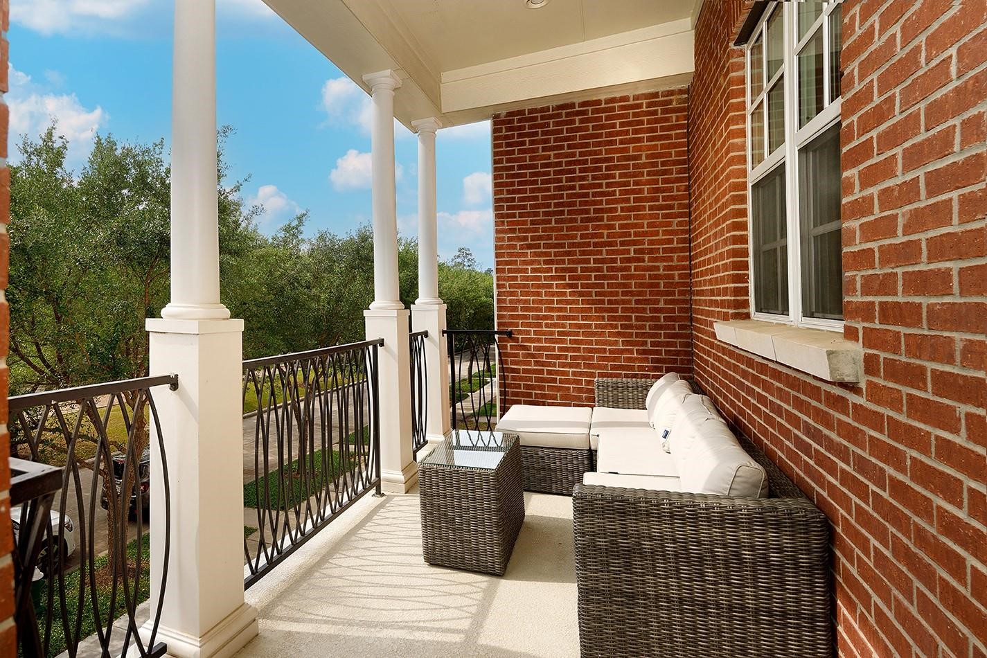 2 Islewood Boulevard Spring, TX 77380 - Photo 3 of 48 A cozy balcony with a brick exterior. The space is partially enclosed with elegant iron railings and offers a view of lush greenery, perfect for relaxation.