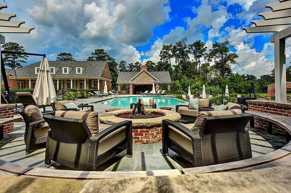 2 Islewood Boulevard Spring, TX 77380 - Photo 41 of 48 East Shore offers an exclusive luxurious outdoor space featuring a large swimming pool, surrounded by elegant seating and umbrellas. The area includes a cozy fire pit with comfortable chairs, set against a backdrop of lush trees and a charming brick community center. Perfect for relaxation and vacation style living.