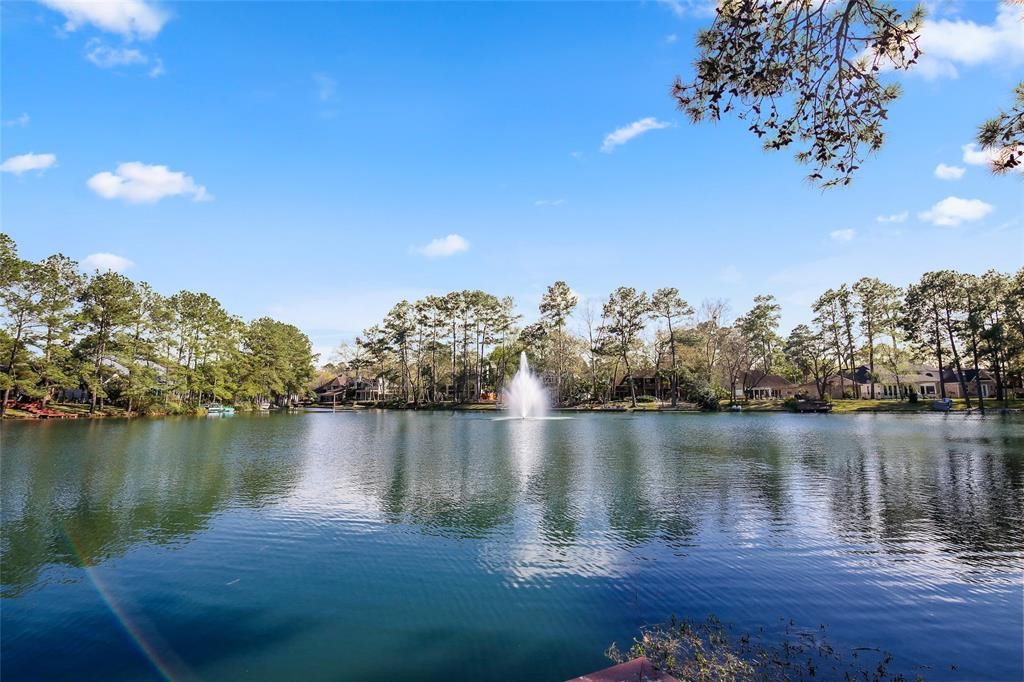 2 Islewood Boulevard Spring, TX 77380 - Photo 47 of 48 The photo showcases a serene lake view with a central fountain, surrounded by lush trees and houses in the background under a clear blue sky. Ideal for those seeking a peaceful, picturesque setting.