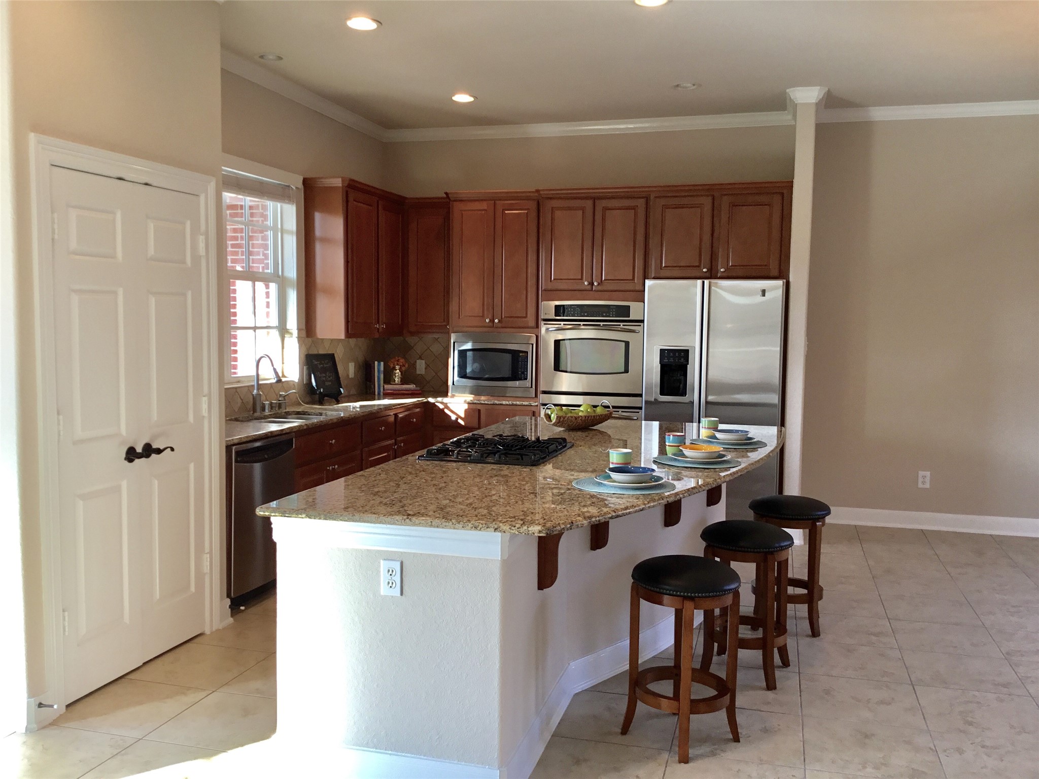 2 Islewood Boulevard Spring, TX 77380 - Photo 6 of 48 The kitchen features granite countertops, stainless steel appliances, and warm wood cabinetry. It includes a central island with a built-in cooktop and spacious countertop seating, offering a modern and functional space.