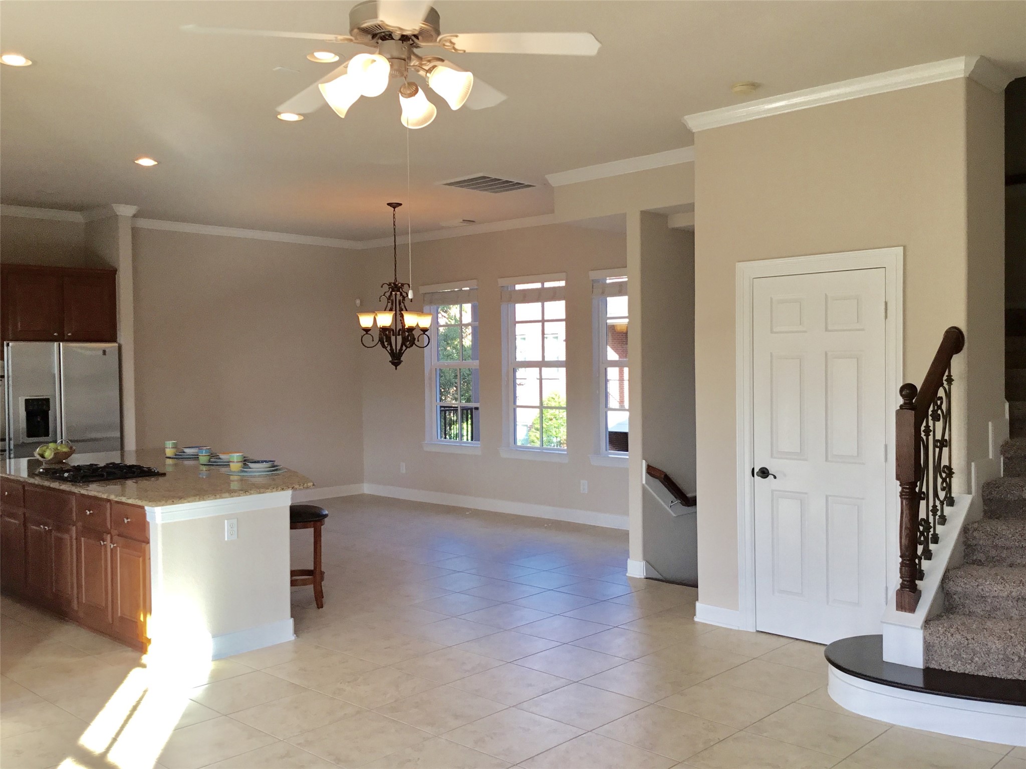2 Islewood Boulevard Spring, TX 77380 - Photo 9 of 48 Bright open-plan living area featuring tiled floors, a modern kitchen with an island and stainless steel appliances, and a cozy dining space under a stylish chandelier. The room boasts large windows for natural light and a staircase with elegant railing.