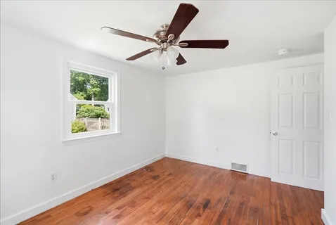 an empty room with wooden floor fan and windows