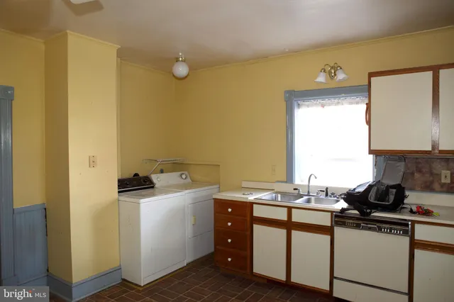 an empty room with wooden floor and way to kitchen