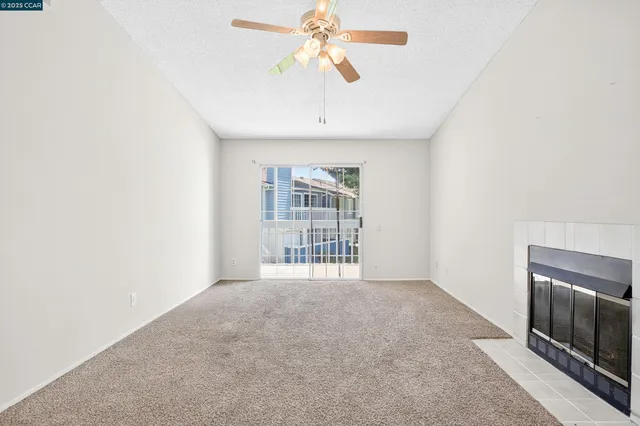 a view of an empty room with chandelier fan and fire place