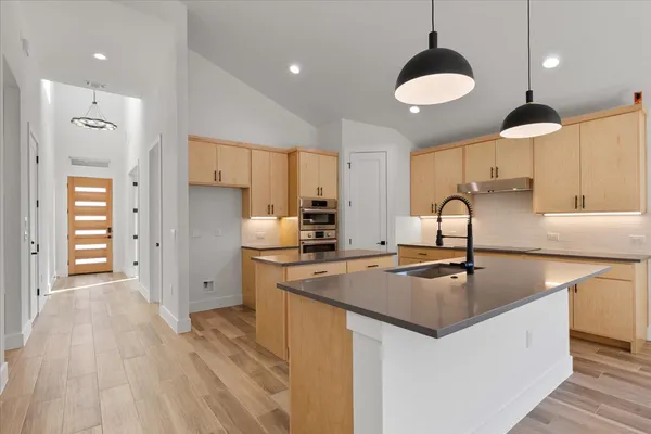 a kitchen with stainless steel appliances granite countertop a sink a stove a refrigerator and island with wooden floor