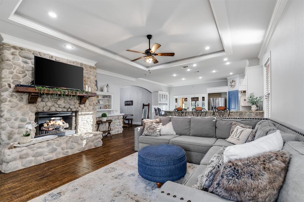 689 Jim Cannon Road Van Alstyne, TX 75495 - Photo 13 of 35 Living area featuring dark wood finished floors, arched walkways, a raised ceiling, a ceiling fan, and a fireplace