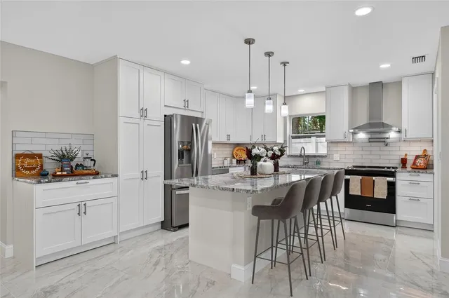 a kitchen with stainless steel appliances kitchen island granite countertop a refrigerator a stove a sink and a dining table with wooden floor