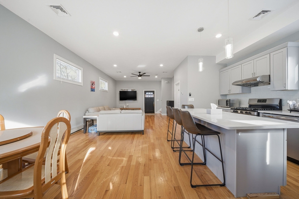 5 Main Street Quincy, MA 02169 - Photo 22 of 42 a kitchen with stainless steel appliances a sink a stove a refrigerator cabinets and a dining table with wooden floor