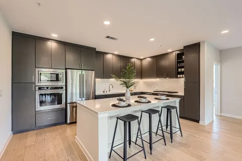 a kitchen with stainless steel appliances kitchen island granite countertop a refrigerator a stove and a sink with wooden floor