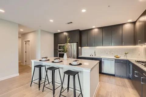 a kitchen with stainless steel appliances kitchen island granite countertop a sink a stove a refrigerator and island with wooden floor