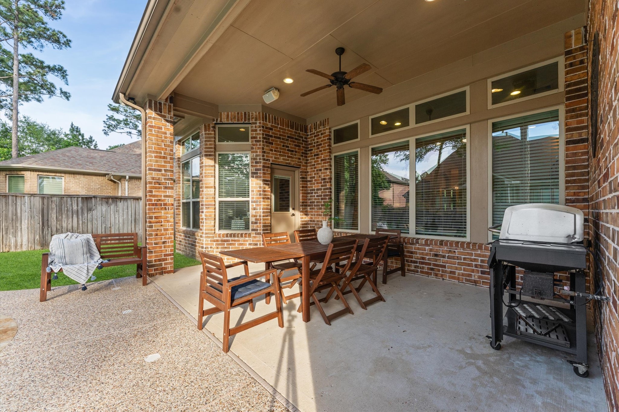 70 Valera Ridge Drive Spring, TX 77389 - Photo 36 of 37 This photo showcases a spacious, covered patio with a ceiling fan and ample seating, perfect for outdoor dining and entertaining. It features a brick exterior, large windows, and a barbecue grill, with a view of a neatly fenced backyard.