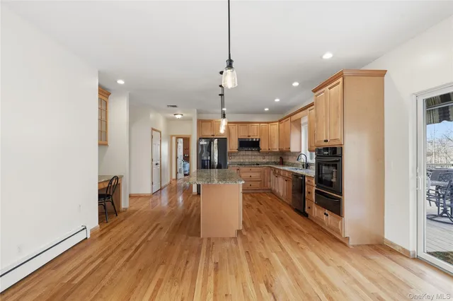 a kitchen with stainless steel appliances kitchen island granite countertop a refrigerator a oven a sink and white cabinets with wooden floor