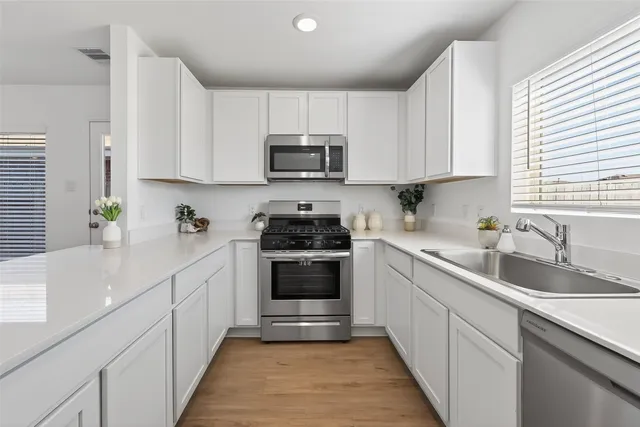 a kitchen with stainless steel appliances granite countertop white cabinets a sink and a window