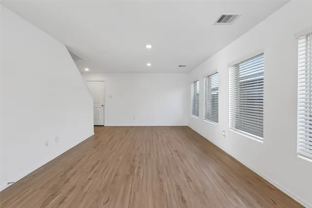 a view of an empty room with wooden floor and window