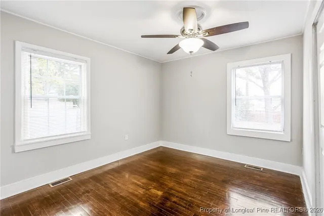 an empty room with wooden floor ceiling fan and windows