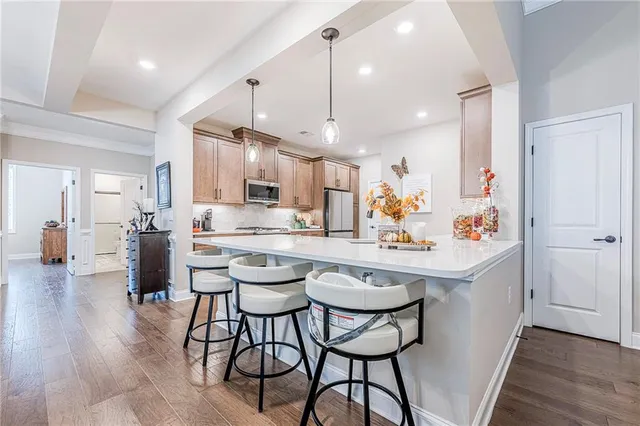 a kitchen with stainless steel appliances kitchen island granite countertop a stove a sink a refrigerator and chairs with wooden floor