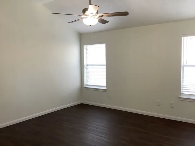 an empty room with wooden floor fan and windows