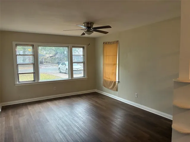 a view of an empty room with wooden floor and a window