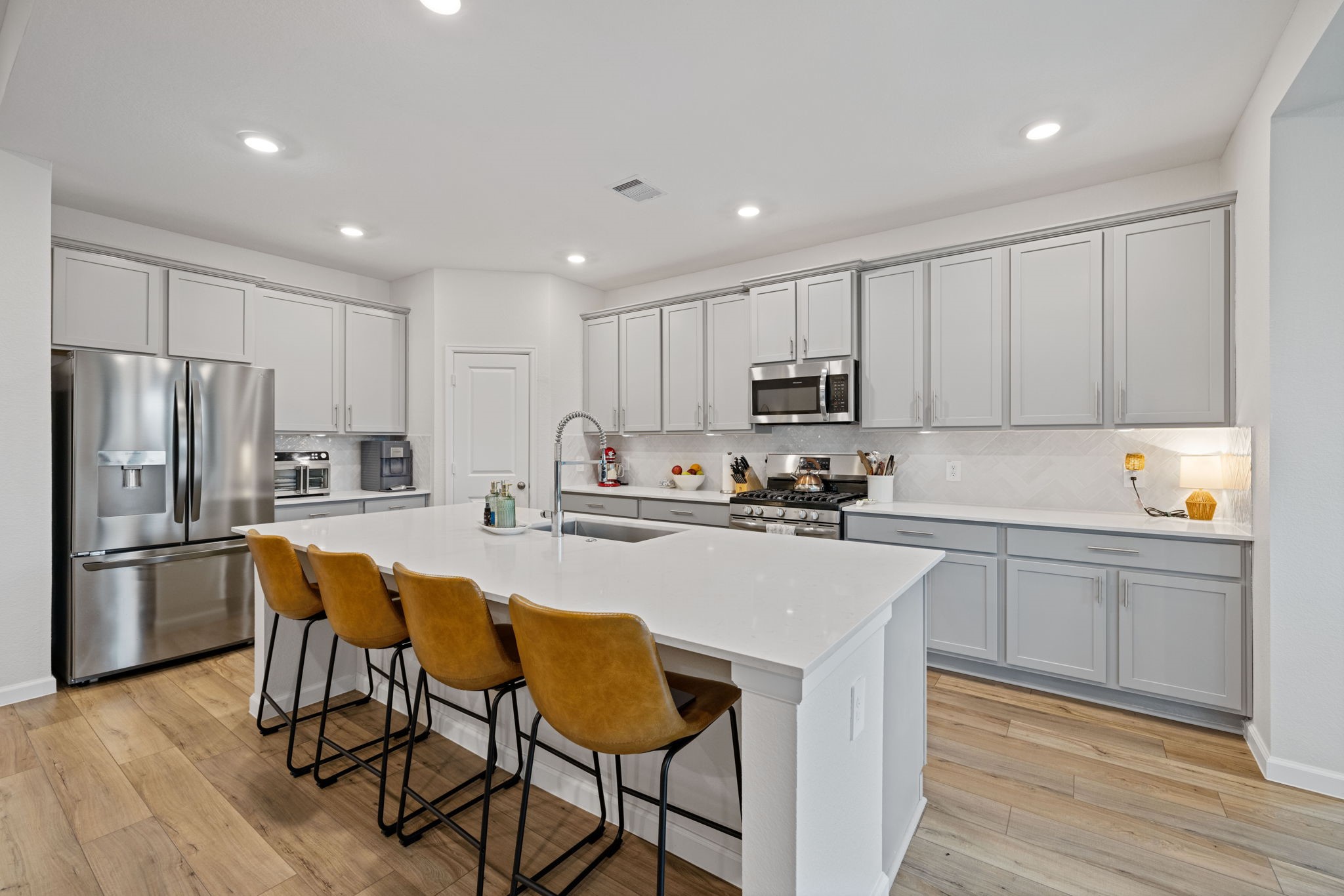 18323 Tiger Flowers Drive Conroe, TX 77302 - Photo 11 of 49 This modern kitchen features sleek stainless steel appliances, ample cabinetry, and a spacious island with bar seating. The light wood flooring and recessed lighting create a bright, inviting atmosphere.
