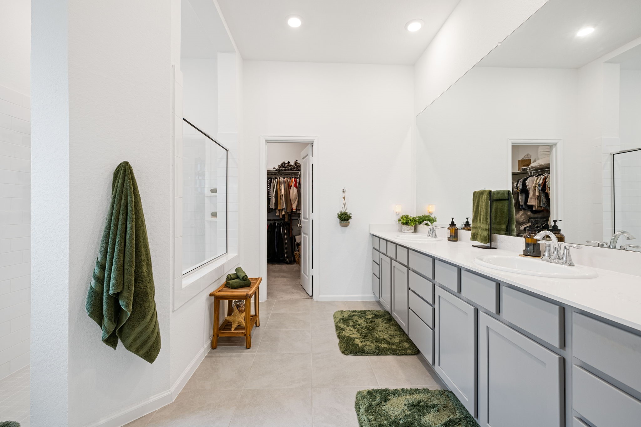 18323 Tiger Flowers Drive Conroe, TX 77302 - Photo 21 of 49 This photo showcases a spacious, modern bathroom with dual sinks, ample storage, and sleek countertops. It features bright lighting, a large mirror, and access to a walk-in closet, creating a luxurious and functional space.