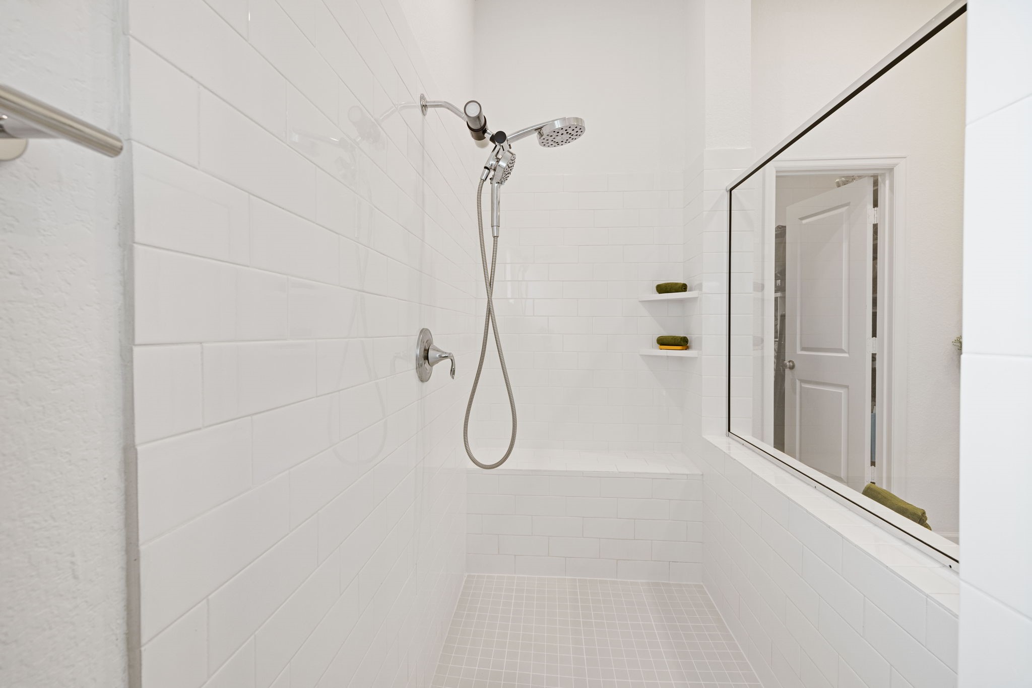 18323 Tiger Flowers Drive Conroe, TX 77302 - Photo 23 of 49 This modern bathroom features a spacious walk-in shower with sleek white tiles, a handheld showerhead, and built-in shelving for storage.