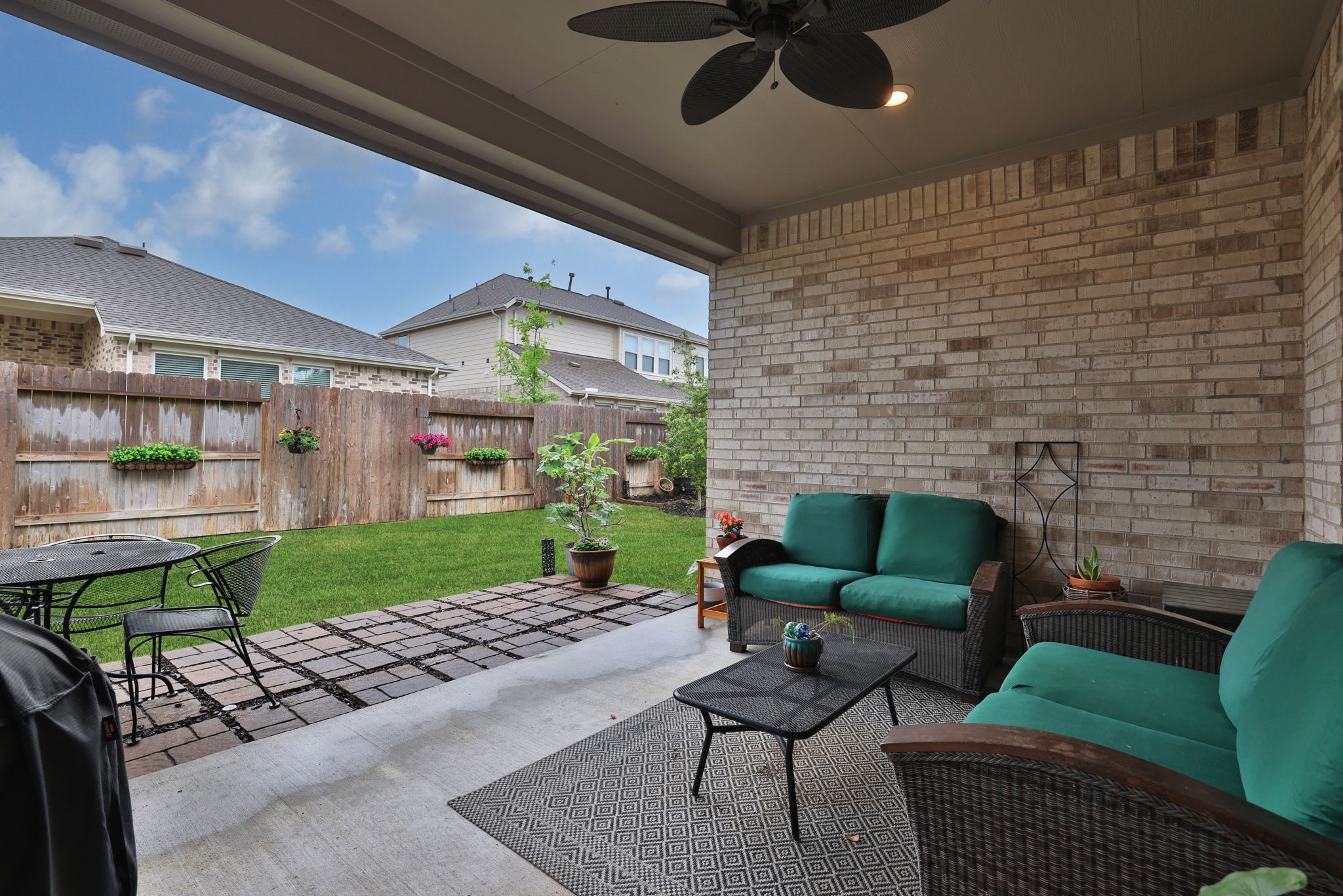 18323 Tiger Flowers Drive Conroe, TX 77302 - Photo 40 of 49 This photo showcases a cozy, covered patio with comfortable seating, a ceiling fan, and a small garden area. The space is inviting and perfect for outdoor relaxation or entertaining.