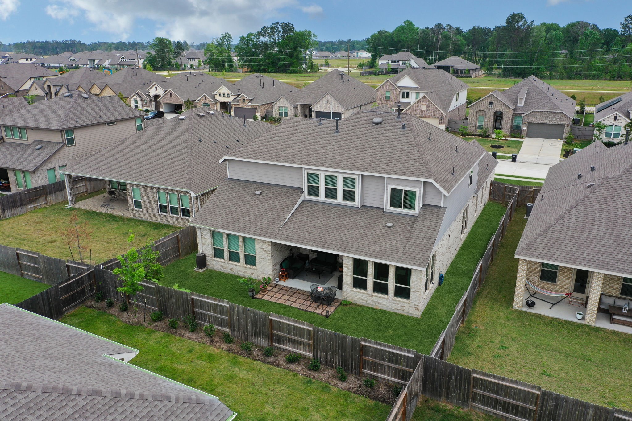 18323 Tiger Flowers Drive Conroe, TX 77302 - Photo 46 of 49 This aerial view showcases a spacious two-story home with a neatly maintained fenced backyard. The property features a large patio area, ideal for outdoor gatherings. The surrounding neighborhood is composed of similar well-kept homes, providing a sense of community.