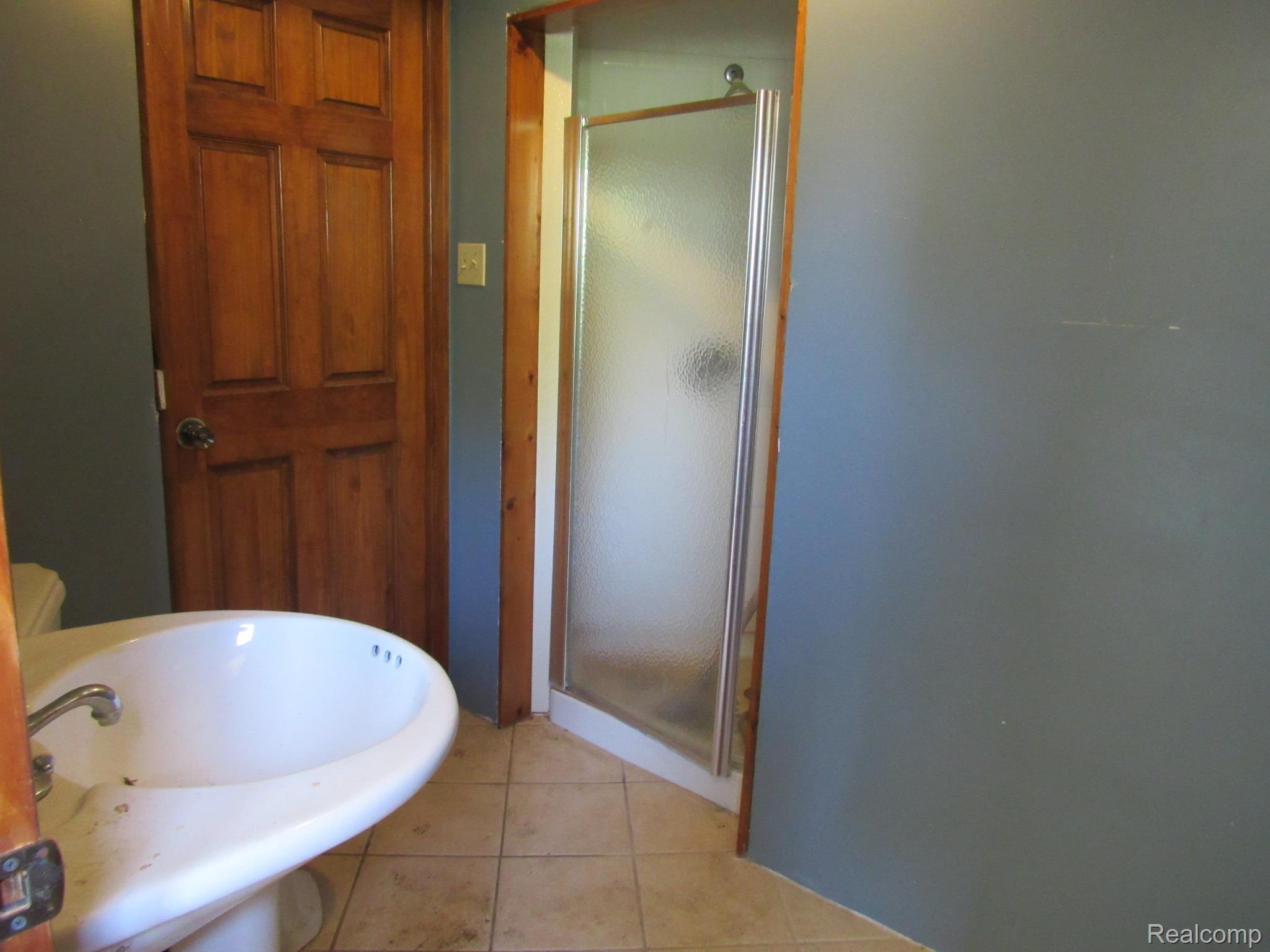 695 Cass Avenue Road Bay City, MI 48708 - Photo 26 of 52 Pedestal sink with chrome faucet, adjacent to a paneled wood-finish door and a standing shower with frosted glass