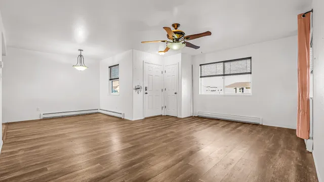an empty room with wooden floor fan and windows