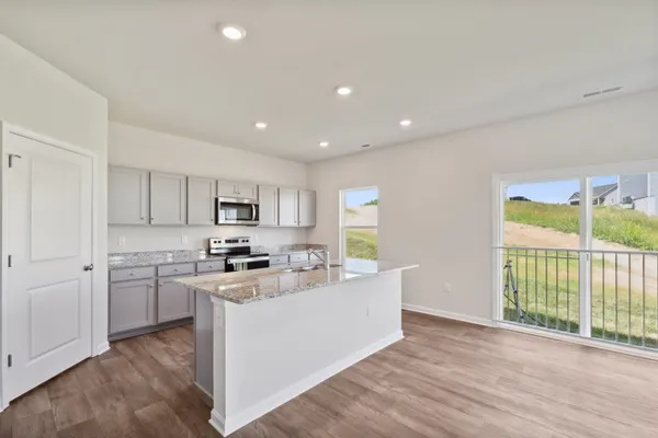 a living room with stainless steel appliances kitchen island granite countertop a stove a sink a refrigerator and white cabinets with wooden floor