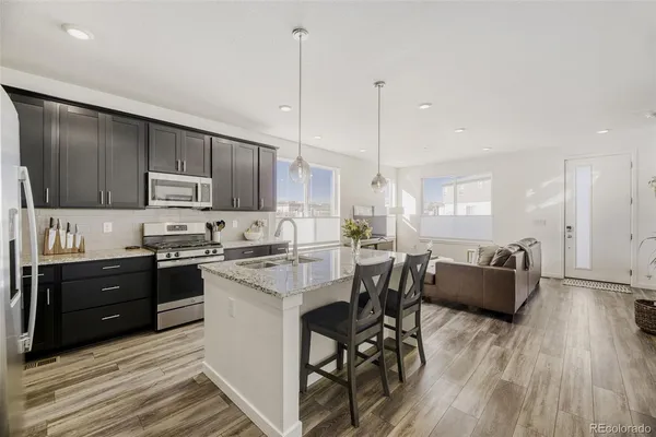 a open kitchen with stainless steel appliances granite countertop a stove top oven a sink dishwasher a dining table and chairs with wooden floor