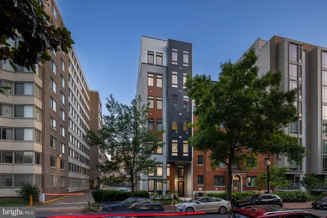 a front view of a building with lot of trees and plants