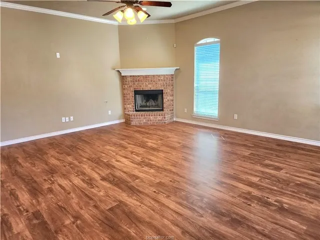 a view of an empty room with wooden floor and a fireplace