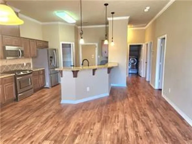 a kitchen with stainless steel appliances kitchen island granite countertop a refrigerator a stove and a wooden floors