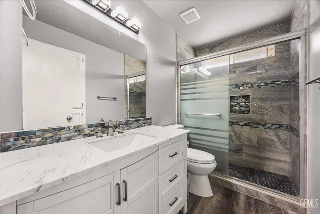 a bathroom with a granite countertop sink a toilet a mirror and shower