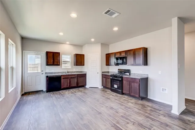 a large kitchen with stainless steel appliances wooden floor and a view of living room