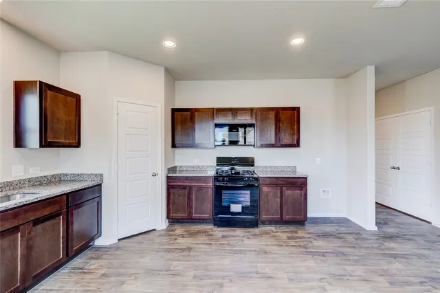 a view of kitchen with stainless steel appliances granite countertop a stove top oven a sink dishwasher and a refrigerator with wooden floor